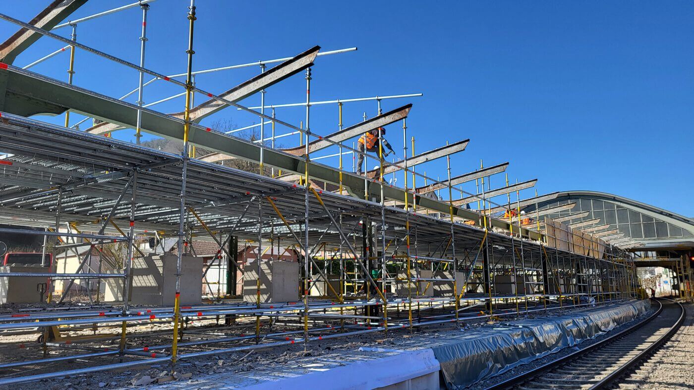 Langer Bahnsteig mit umfangreichem Gerüst, Bauarbeiter auf der oberen Ebene, Gleise rechts.
